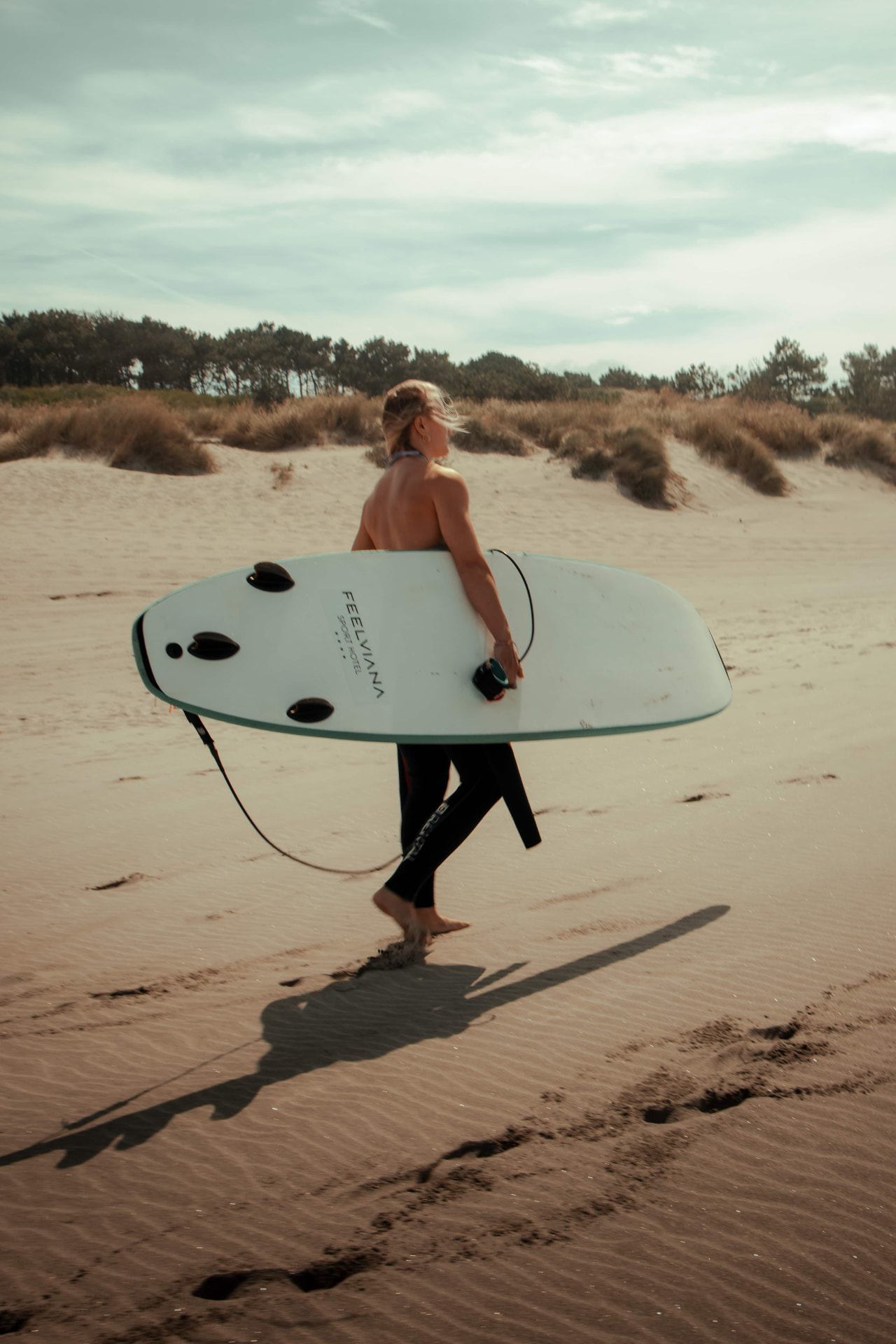 A guest carrying a surfboard across the dunes